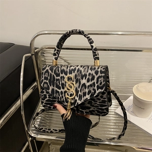 Sac bandoulière chic léopard avec logo S doré et gland sur un support en verre élégant