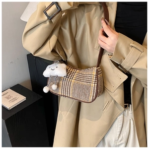 Detail of checkered shoulder bag with plush cloud charm on a khaki trench coat