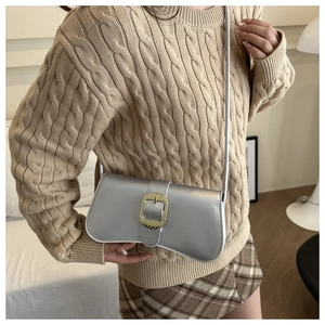 Close-up of a metallic silver crossbody bag with a large textured gold buckle detail