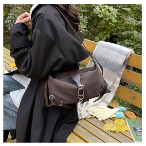 Detail of dark brown matte shoulder bag with silver metal ring on model in autumn park