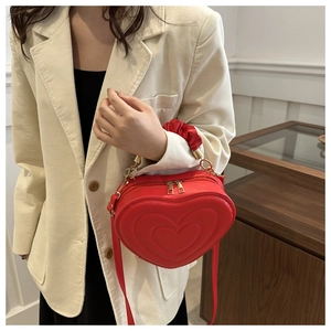 Detail of red heart-shaped bag with embossed pattern and ruched handle on white blazer
