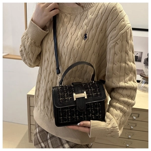Detail view of black tweed handbag with golden H-clasp and leather crossbody strap
