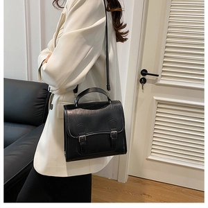 Detail of classic black buckle briefcase bag worn over the shoulder in a minimalist room