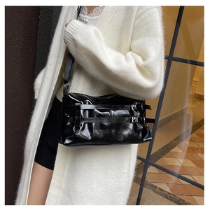 Detail der schwarzen Lackleder-Schultertasche mit dekorativen Schnallenriemen an einem Modell