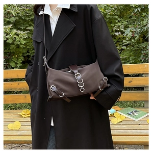 Outdoor shot of a brown vintage crossbody bag with silver buckles on a black trench coat