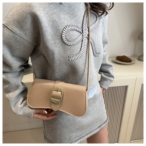 Close-up of beige leather shoulder bag with a large golden woven metal clasp on person
