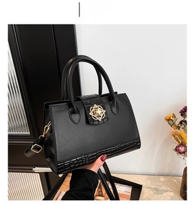 Detail of black faux leather handbag with crocodile pattern and golden flower buckle