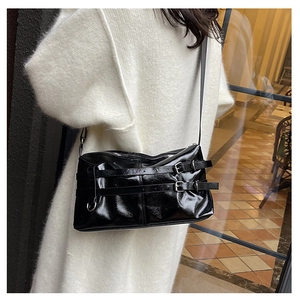 Close-up of black glossy patent leather shoulder bag with silver belt buckle details