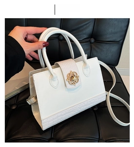 Detail of white handbag with gold flower clasp and crocodile texture on black background