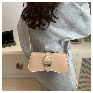 Close-up of a beige shoulder bag featuring a textured gold square buckle on the flap