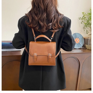 Detail of vintage brown leather backpack with double buckles and top handle on black blazer