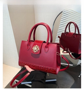 Close-up of red crocodile embossed PU leather handbag with golden floral lock and strap