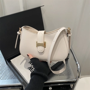 Cream white crescent underarm bag with gold buckle and adjustable strap on a minimalist display
