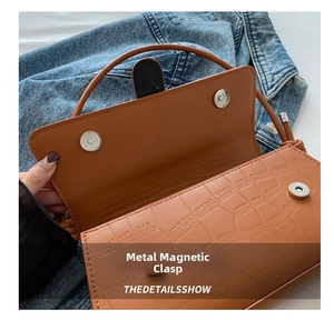 Detail of a brown crocodile pattern shoulder bag featuring a silver magnetic clasp closure