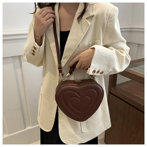 Close-up of brown heart-shaped bag with layered embossing and pleated handle on a model