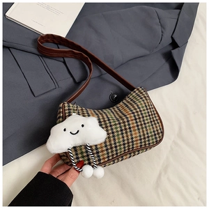 Detail view of plaid woolen underarm bag with leather trim and plush smile charm