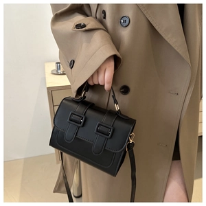 Classic black crossbody bag with adjustable strap and decorative buckles on a trench coat
