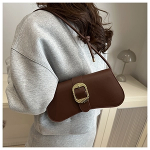 Detail of dark brown leather underarm bag with a large golden textured square buckle