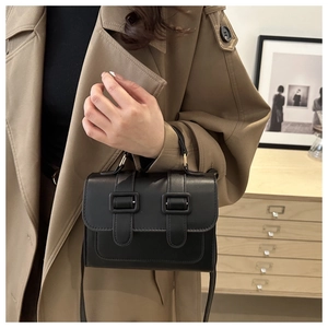 Detail shot of a black flap crossbody bag styled with a trench coat in a cozy room