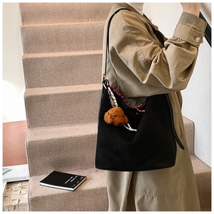 Details of a black suede tote bag with a teddy bear charm and woven shoulder strap