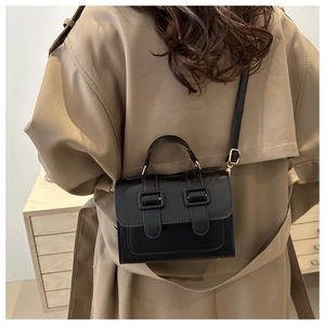 Classic black leather square bag with double buckles shown on a beige coat model