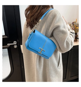 Détail d'un sac à bandoulière en cuir bleu vif avec logo T en métal et chaîne dorée