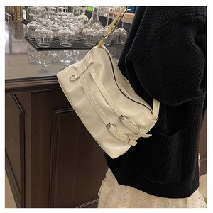 Detail of white patent leather shoulder bag featuring decorative buckle straps and silver hardware