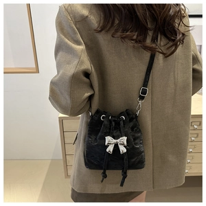 Fashionable black drawstring bucket bag with silver bow accent and adjustable shoulder strap