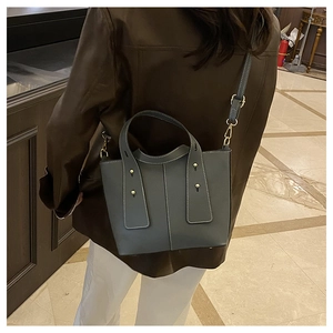 Side view of gray-blue bucket bag featuring white contrast stitching and gold rivets