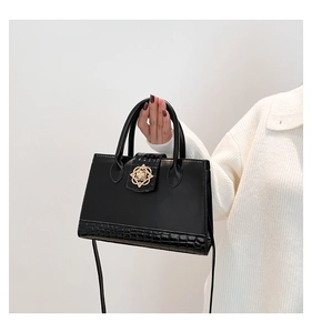 Detail of black crossbody bag with gold flower buckle and crocodile texture accents