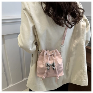 Detailed view of pink drawstring bucket bag with silver bow on model in corduroy blazer