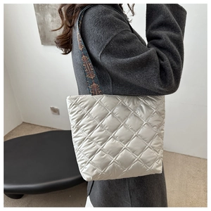 Detail of silver quilted tote bag with colorful ethnic embroidered shoulder strap on a coat