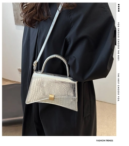 Detail showing silver crocodile-embossed texture and curved base on a small crossbody bag