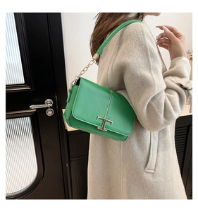 Détail du sac à rabat en cuir vert avec boucle en T dorée et bandoulière en chaîne