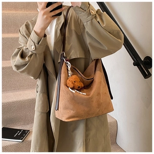 Detail of brown suede tote bag with puppy charm and slim straps on khaki trench coat
