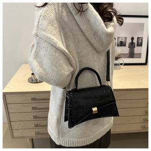 Detail of black crocodile texture bag with gold metal buckle on a beige sweater
