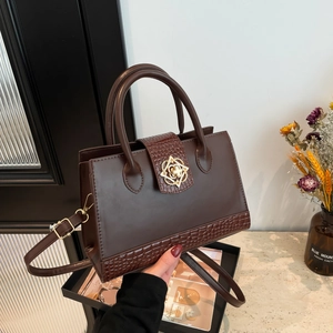 Dark brown crocodile embossed crossbody bag with golden floral buckle held by a model