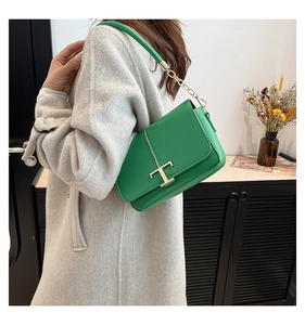Détail d'un sac en cuir vert avec fermoir doré en T porté sur un manteau gris