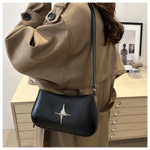 Détail d'un sac bandoulière noir en forme de lune avec étoile argentée sur un trench-coat