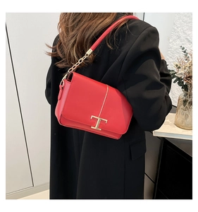 Détail du sac en cuir rouge avec fermoir doré en T et bandoulière chaîne élégante