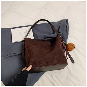 Detail of dark brown suede tote bag with plush puppy charm and smooth leather bottom trim