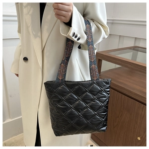 Detail of black quilted handbag featuring a bohemian geometric woven handle on a white coat