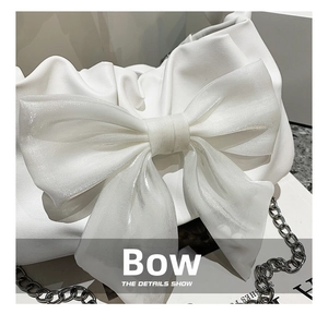 Macro view of white leather handbag with oversized bow detail and silver chain strap