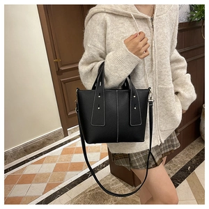 Detail of black pebbled leather tote bag with white contrast stitching and shoulder strap