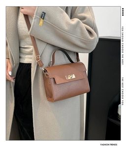 Detail of a brown leather crossbody bag featuring a gold twist lock and fine grain texture