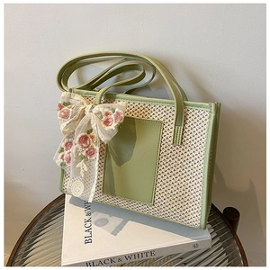 Detail of woven straw tote bag with green leather trim and floral lace bow decoration