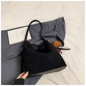 Detail of black suede tote bag featuring a leather base and a brown dog plush charm