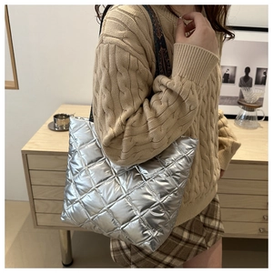 Detail of silver quilted puffer tote bag with ethnic pattern strap on shoulder