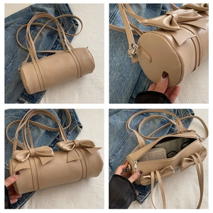 Detail view of beige cylindrical shoulder bag featuring dual bows and spacious interior