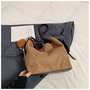 Brown suede hobo tote bag with plush bear charm and scarf on a white bedsheet background